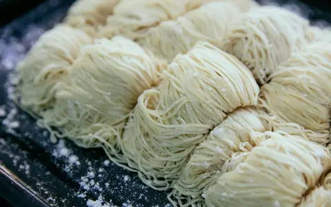 Surowe, cienkie nitki makaronu ułożone w porcje na ciemnej tacy. Czy pies może jeść makaron?