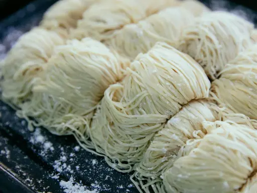 Surowe, cienkie nitki makaronu ułożone w porcje na ciemnej tacy. Czy pies może jeść makaron?