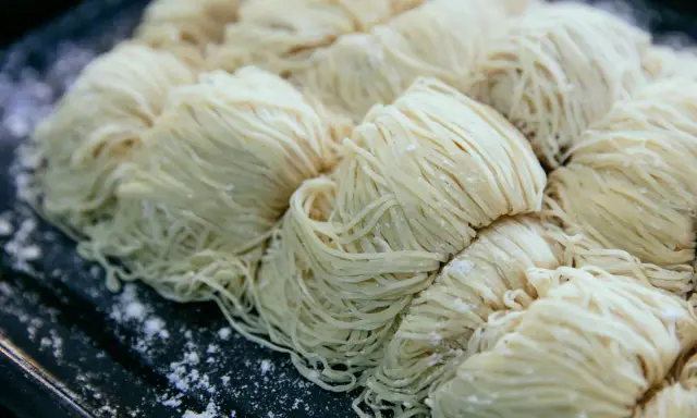 Surowe, cienkie nitki makaronu ułożone w porcje na ciemnej tacy. Czy pies może jeść makaron?